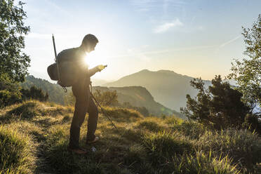 Silhouette eines Mannes, der ein Mobiltelefon benutzt, während er auf einem Berg vor dem Himmel steht, Orobie, Lecco, Italien - MCVF00586