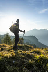 Silhouette eines männlichen Wanderers, der während des Sonnenaufgangs auf einem Berg steht und die Aussicht betrachtet, Orobie, Lecco, Italien - MCVF00587