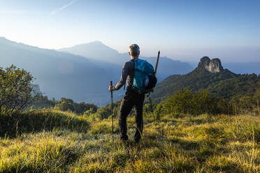 Männlicher Wanderer mit Rucksack, der bei Sonnenaufgang den Berg gegen den Himmel betrachtet, Orobie, Lecco, Italien - MCVF00590