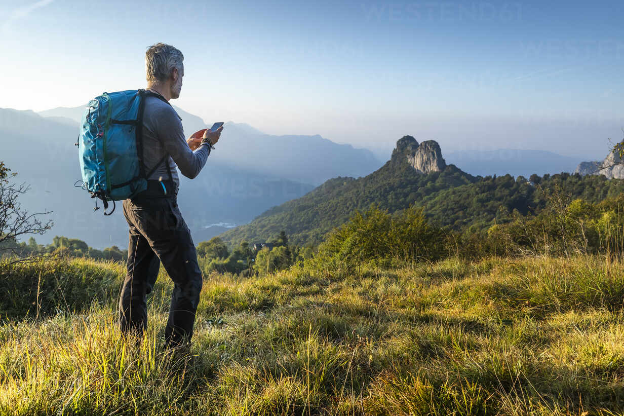 Mature man using smart phone while hiking on mountain at sunrise, Orobie,  Lecco, Italy stock photo