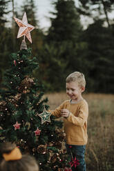 Lächelnder Junge beim Schmücken des Weihnachtsbaums in der Natur stehend - GMLF00602