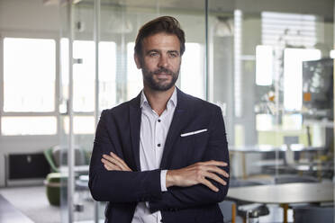 Confident businessman with arms crossed standing at office - RBF07880