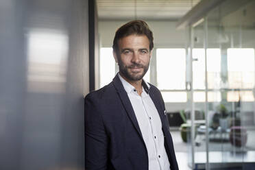 Businessman leaning on wall at office - RBF07883