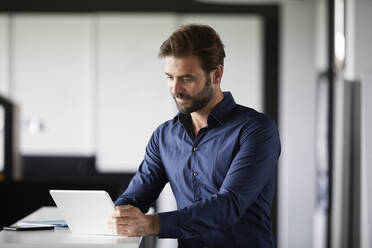 Geschäftsmann, der ein digitales Tablet benutzt, während er am Schreibtisch im Büro steht - RBF07889