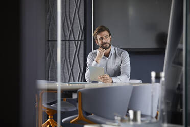 Nachdenklicher Geschäftsmann hält digitale Tabelle, während er im Büro sitzt - RBF07901