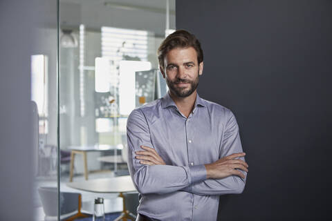 Confident businessman with arms crossed standing in office stock photo