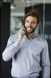 Businessman smiling while talking on mobile phone in office - RBF07915