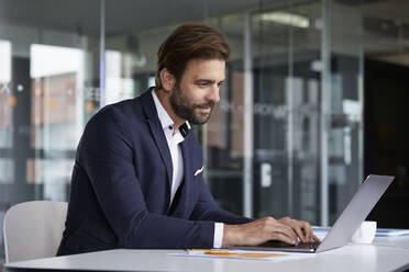 Geschäftsmann arbeitet am Laptop im Büro sitzend - RBF07918