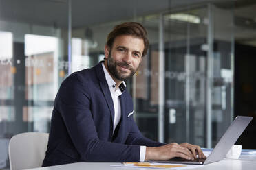 Businessman working on laptop while sitting by desk in office - RBF07923