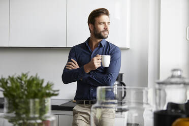 Man drinking coffee standing at cafeteria in office - RBF07934