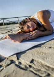 Junge Frau mit geschlossenen Augen, die auf einer Matte gegen den klaren Himmel bei Sonnenuntergang trainiert - MGOF04425
