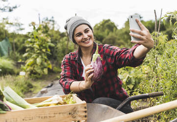 Junge Frau nimmt Selfie mit Aubergine im Gemüsegarten - UUF21447