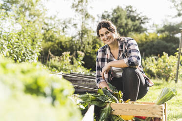 Smiling young woman working while crouching in vegetable garden - UUF21461