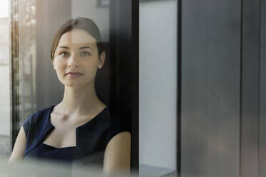 Nahaufnahme einer selbstbewussten Geschäftsfrau an der Wand eines Büros, gesehen durch eine Glastür - BMOF00414