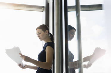 Unternehmerin analysiert Berichte, während sie im Büro am Fenster steht - BMOF00417