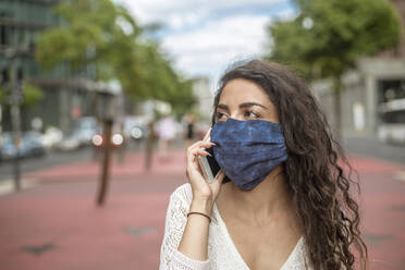 Close-up of young woman wearing mask talking over mobile phone in city - BFRF02293