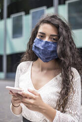 Close-up of woman wearing face mask using smart phone while standing in city - BFRF02297