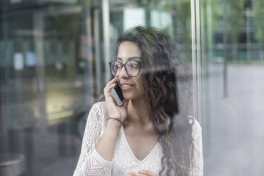 Nahaufnahme einer Frau mit langen Haaren, die am Fenster stehend über ein Mobiltelefon spricht - BFRF02300