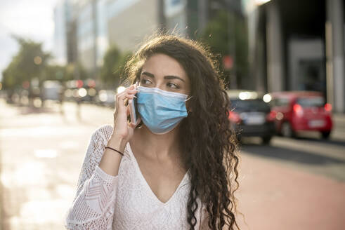 Close-up of young woman wearing mask talking over mobile phone on street in city - BFRF02305