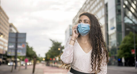 Woman wearing mask talking over mobile phone while standing in city stock photo