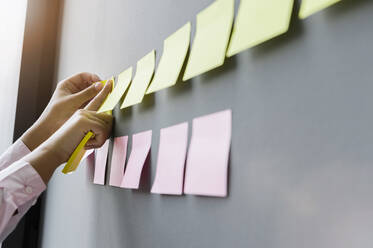 Hands of businesswoman sticking adhesive notes on wall in office - BMOF00419