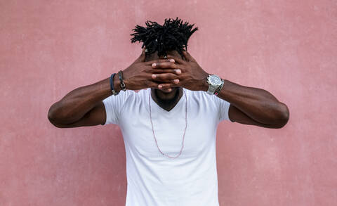 Mid adult man with hands covering eyes while standing against pink wall stock photo