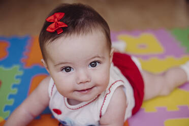 Close-up of cute smiling baby girl lying on puzzle playmat at home - EBBF00752