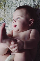 Close-up of shirtless baby girl sticking out tongue while lying on bed at home - EBBF00761