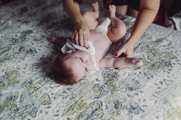 Hands of mother dressing up baby daughter lying on bed at home - EBBF00763