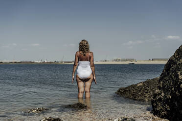 Senior woman wearing swimwear standing in sea against sky during sunny day - ERRF04380