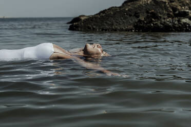 Ältere Frau mit geschlossenen Augen schwimmt auf dem Meer an einem sonnigen Tag - ERRF04384