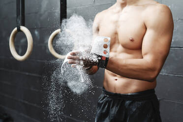 Close-up of shirtless young man dusting sports chalk with hands in gym - JCZF00224