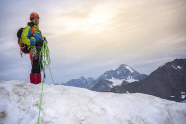 Mature man holding ropes while standing on snowcapped mountain against sky, Stelvio National Park, Italy - MCVF00601