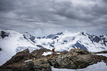 Älterer Mann steht auf einem Felsen vor bewölktem Himmel, Nationalpark Stilfser Joch, Italien - MCVF00604