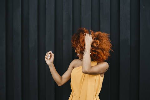 Cheerful young woman shaking hair while standing against wall stock photo