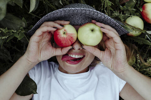 Close-up of cheerful woman holding apples in front of eyes while lying at in orchard stock photo
