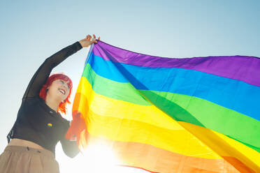 Young girl raising LGBT flag in street in daylight - CAVF89105