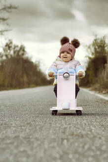 Ein 1 Jahr altes Baby-Mädchen ist mit einem rosa Motorrad draußen - CAVF89111