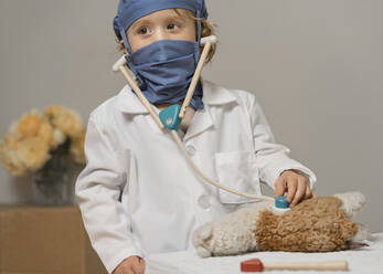 Young child in medical PPE examines a plush toy lama - CAVF89114