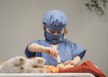 Ein kleines Kind, das eine medizinische PSA trägt, untersucht eine Babypuppe, indem es ihre Temperatur mit einem Thermometer misst - CAVF89121