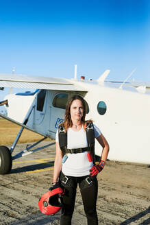 Junge Fallschirmspringerin mit Rucksack auf einem Flugplatz mit Flugzeug - CAVF89131