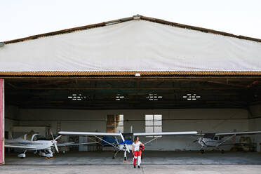 Junge Fallschirmspringerin in einem Flugzeughangar, umgeben von Flugzeugen - CAVF89140