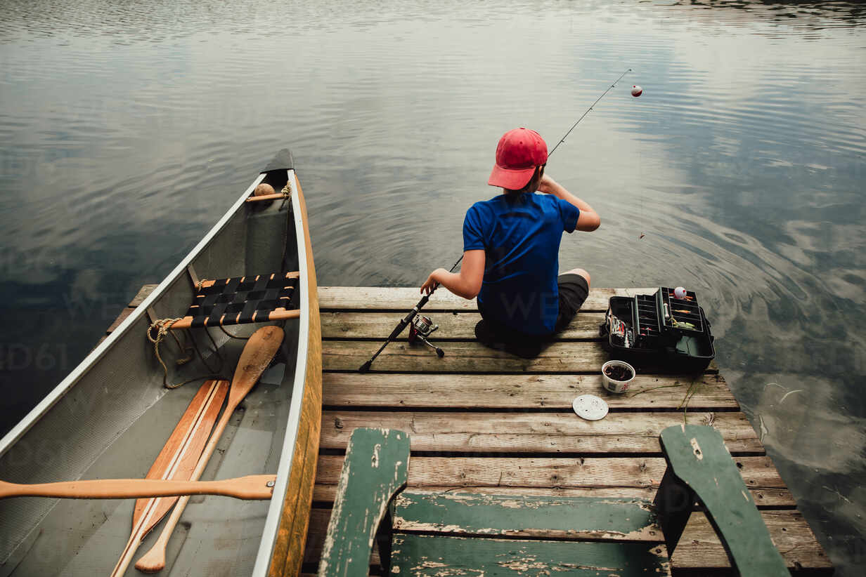 Teen boy fishing from a dock on a lake with tackle box in the summer. stock  photo