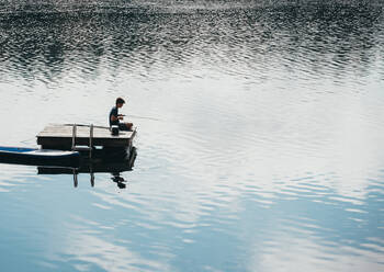 Jugendlicher beim Angeln von einer Badeplattform an einem See im Sommer. - CAVF89151