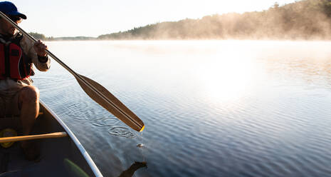 Ein Mann paddelt morgens mit seinem Kanu auf einem nebligen See in Ontario, Kanada. - CAVF89158