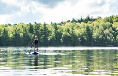 Ein Jugendlicher paddelt auf einem SUP auf einem See in Ontario, Kanada, an einem sonnigen Tag. - CAVF89165