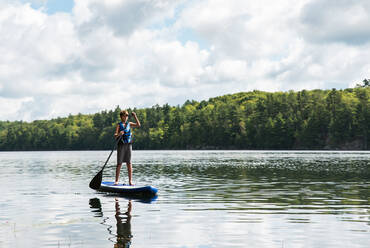 Ein Jugendlicher paddelt auf einem SUP auf einem See in Ontario, Kanada, an einem sonnigen Tag. - CAVF89166