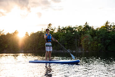 Ein Jugendlicher paddelt auf einem SUP auf einem See in Ontario, Kanada, an einem sonnigen Tag. - CAVF89170