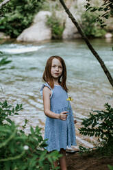 Vertikales Porträt eines jungen Mädchens, das eine Blume neben einem Fluss hält - CAVF89202