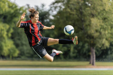 Junge Frau spielt Fußball auf einem Feld - STSF02608